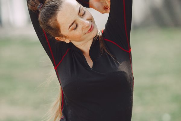Une adulte en tenue de sport étire ses bras au-dessus de la tête, à l’extérieur.
