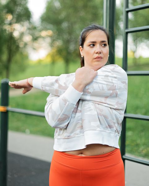 Une adulte étire doucement un bras devant elle dans un parc.